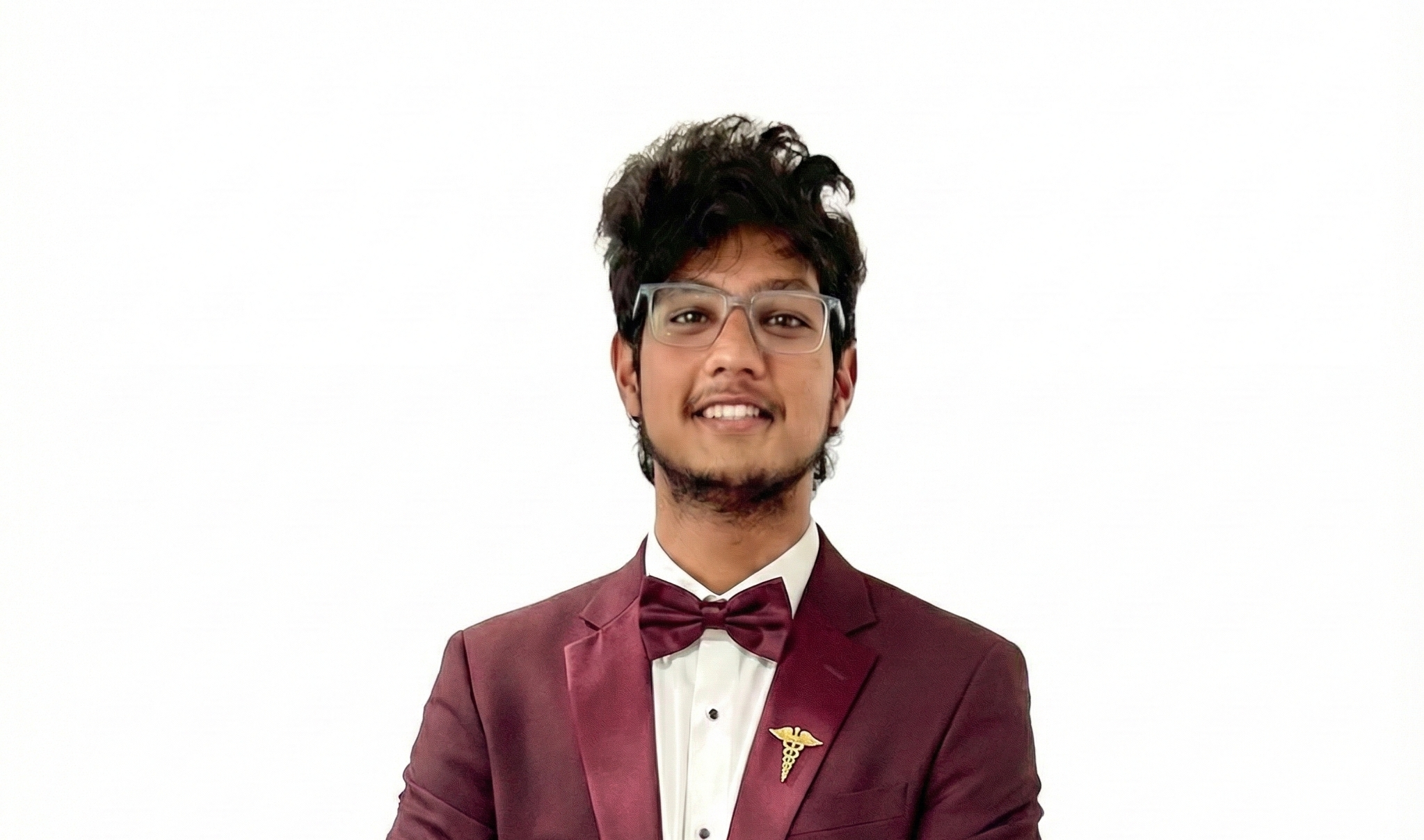 Portrait of Praneeth Roy in a maroon suit with a caduceus pin